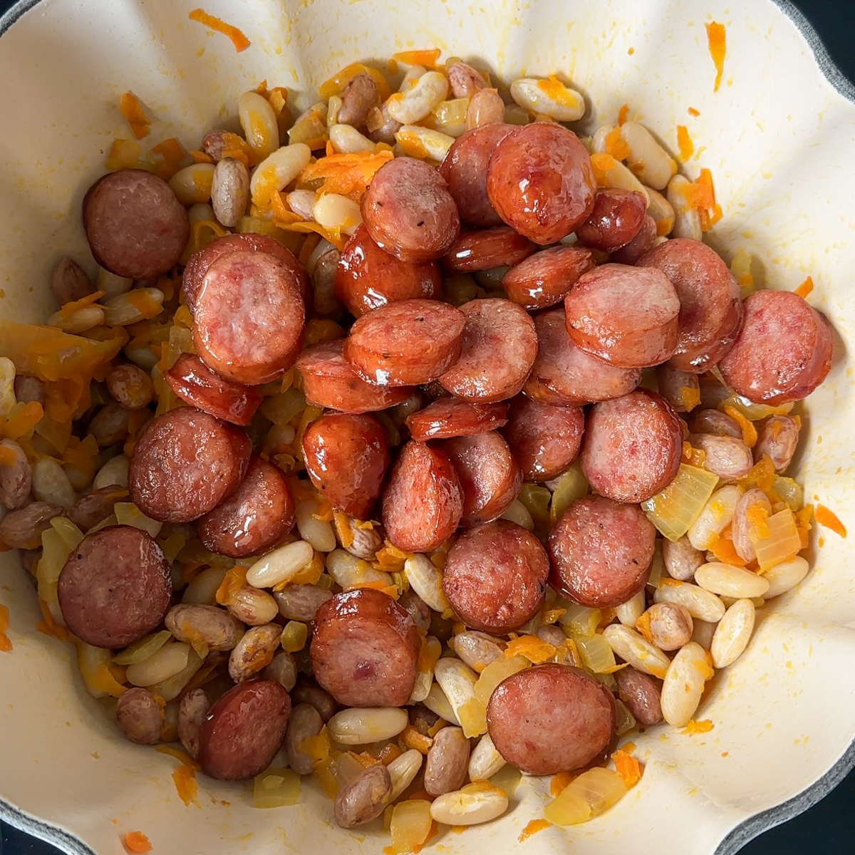 Sauté onions, carrots & add in sausage, beans & water.