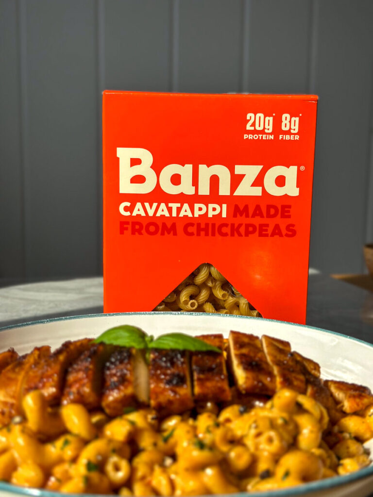Close up of creamy chicken pasta with sliced chicken, with a box of Banza chickpea cavatappi behind it
