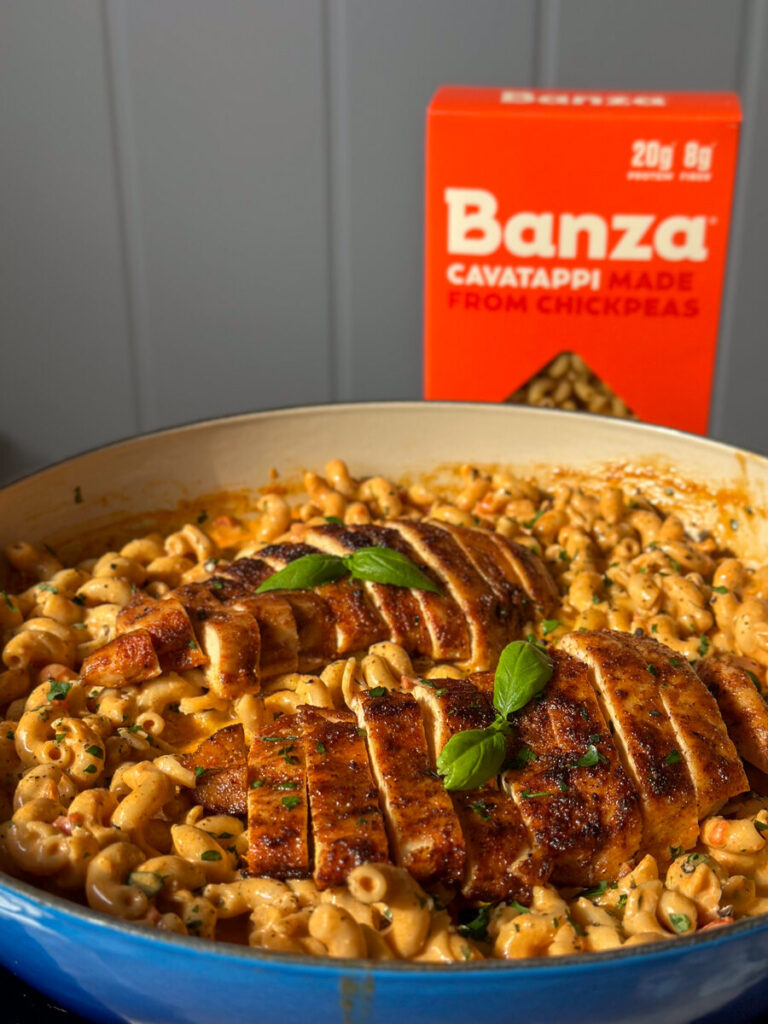 Skillet of creamy chicken pasta topped with two sliced chicken breasts and fresh basil